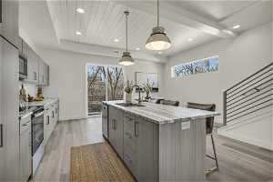 Kitchen with a breakfast bar area, a center island with sink, stainless steel appliances, light hardwood / wood-style floors, and decorative light fixtures