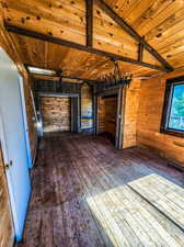 Interior space with wood walls, lofted ceiling with beams, wood ceiling, and dark hardwood / wood-style flooring