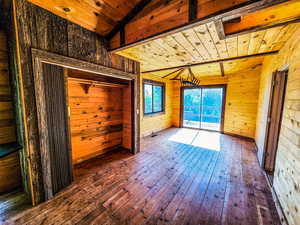 Unfurnished room featuring wooden walls, wooden ceiling, dark wood-type flooring, and lofted ceiling