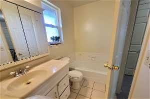 Bathroom featuring toilet, tile floors, vanity with extensive cabinet space, and a bathtub