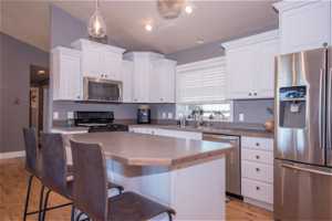 Kitchen featuring light hardwood / wood-style flooring, a breakfast bar area, stainless steel appliances, decorative light fixtures, and white cabinetry