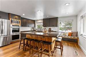 Kitchen with a breakfast bar, light wood-type flooring, stainless steel appliances, and tasteful backsplash
