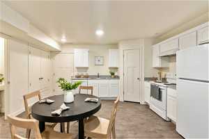 Kitchen with white appliances, white cabinetry, light wood-type flooring, and custom range hood