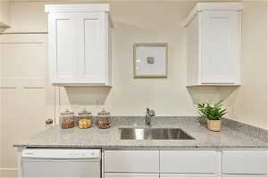 Kitchen with sink, white cabinetry, light stone counters, and dishwasher