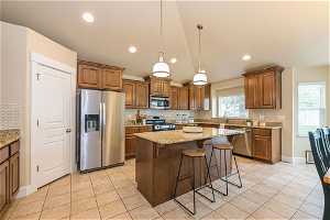 Kitchen with a center island, appliances with stainless steel finishes, backsplash, hanging light fixtures, and light stone counters