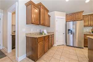 Kitchen featuring backsplash, light tile flooring, stainless steel refrigerator with ice dispenser, and light stone counters