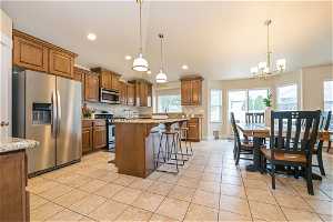 Kitchen featuring pendant lighting, light tile floors, a chandelier, stainless steel appliances, and a kitchen bar