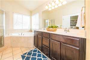 Bathroom featuring independent shower and bath, tile floors, vaulted ceiling, and dual bowl vanity