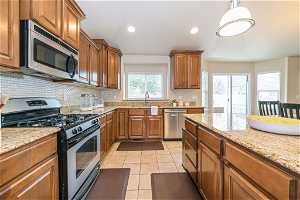 Kitchen featuring decorative light fixtures, backsplash, stainless steel appliances, light tile floors, and light stone counters
