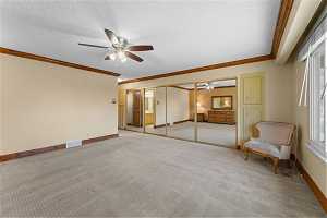 Interior space with ceiling fan, a textured ceiling, and crown molding