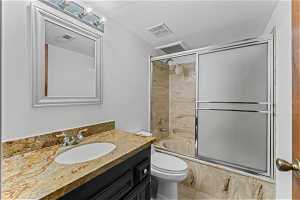 Full bathroom featuring a textured ceiling, tile flooring, toilet, oversized vanity, and enclosed tub / shower combo