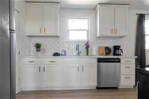 Kitchen featuring sink, light wood-type flooring, white cabinets, stainless steel dishwasher, and tasteful backsplash