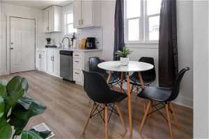 Kitchen with light hardwood / wood-style flooring, white cabinets, backsplash, dishwasher, and sink