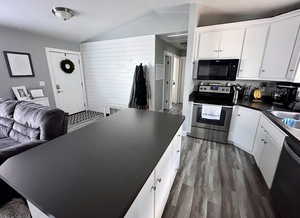 Kitchen featuring white cabinets, dark wood-type flooring, vaulted ceiling, and stainless steel appliances