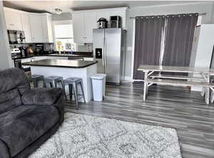 Kitchen featuring dark hardwood / wood-style floors, a kitchen breakfast bar, white cabinets, stainless steel appliances, and a center island