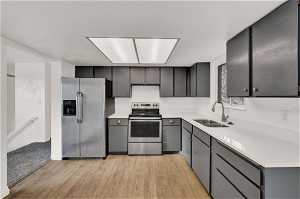 Kitchen with light hardwood / wood-style floors, appliances with stainless steel finishes, gray cabinets, and sink