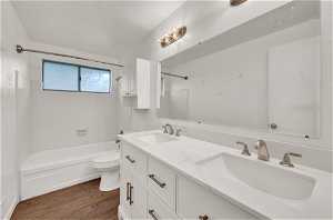 Full bathroom featuring tiled shower / bath, toilet, double sink vanity, and hardwood / wood-style flooring