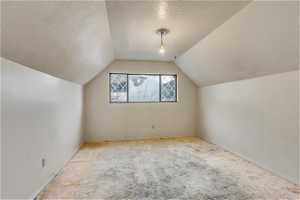 Bonus room with a textured ceiling, light colored carpet, and lofted ceiling