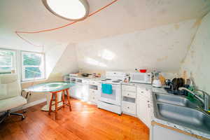 Kitchen with white cabinetry, white appliances, sink, light wood-type flooring, and vaulted ceiling