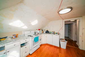 Kitchen featuring light wood-style floors, vaulted ceiling, white appliances, white cabinets, and sink