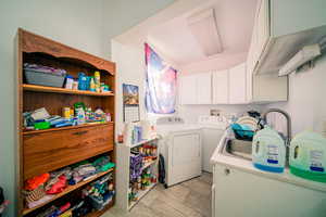 Clothes washing area with washer hookup, washing machine and dryer, light tile floors, and cabinets