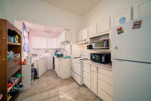 Kitchen featuring white appliances, sink, light tile floors, washer and clothes dryer, and white cabinets