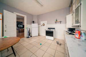 Kitchen with white appliances, a textured ceiling, white cabinetry, and light wood-type flooring