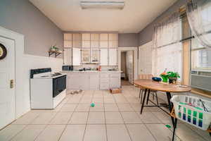 Kitchen with light tile floors, white cabinetry, and electric range