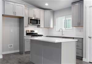 Kitchen with gray cabinetry, dark wood-type flooring, sink, stainless steel appliances, and tasteful backsplash