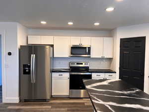 Kitchen featuring white cabinetry, dark hardwood / wood-style floors, backsplash, and stainless steel appliances