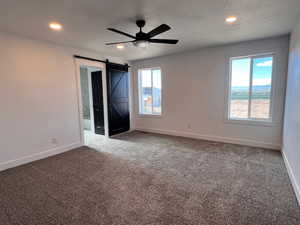 Spare room with a barn door, carpet flooring, and ceiling fan