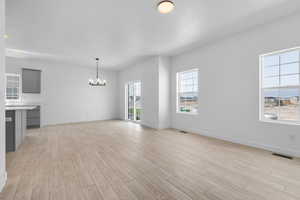 Unfurnished living room featuring an inviting chandelier, light wood-type flooring, and a wealth of natural light