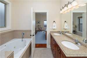 Bathroom with a relaxing tiled bath, dual sinks, vanity with extensive cabinet space, and tile flooring
