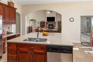 Kitchen with ceiling fan, a fireplace, sink, light tile floors, and stainless steel dishwasher