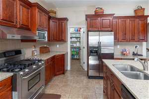 Kitchen with stainless steel appliances, light tile flooring, light stone countertops, backsplash, and sink