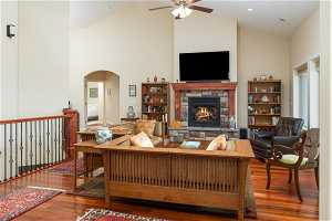 Living room featuring ceiling fan, a stone fireplace, dark wood-type flooring, and high vaulted ceiling