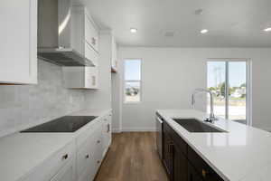 Kitchen with wall chimney exhaust hood, light stone countertops, hardwood / wood-style floors, and sink