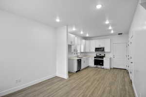 Kitchen with appliances with stainless steel finishes, white cabinetry, sink, and light wood-type flooring