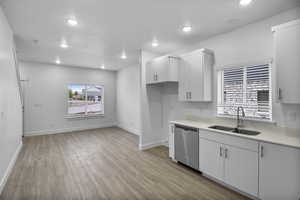 Kitchen with white cabinetry, light hardwood / wood-style floors, sink, and stainless steel dishwasher