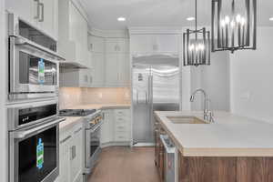 Kitchen featuring tasteful backsplash, high end appliances, white cabinets, sink, and wood-type flooring