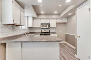 Kitchen featuring stainless steel appliances, kitchen peninsula, white cabinetry, and new flooring.