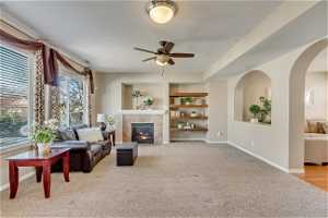 Living room featuring built in features, ceiling fan, light carpet, and a tile fireplace