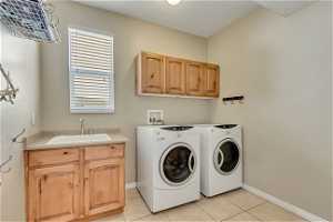 Clothes washing area with cabinets, separate washer and dryer, sink, and light tile floors