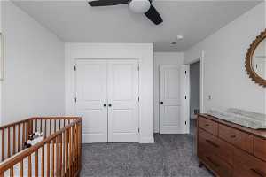 Carpeted bedroom featuring a closet, a nursery area, and ceiling fan