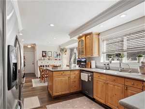 Kitchen with stainless steel appliances, kitchen peninsula, ornamental molding, dark hardwood / wood-style flooring, and sink