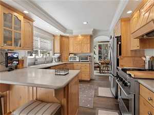 Kitchen featuring dark hardwood / wood-style floors, appliances with stainless steel finishes, light brown cabinets, custom range hood, and ornamental molding