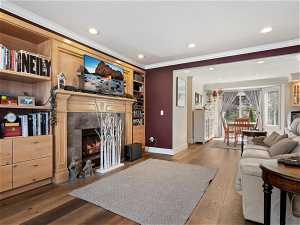 Living room featuring a tiled fireplace, light hardwood / wood-style floors, built in features, and ornamental molding