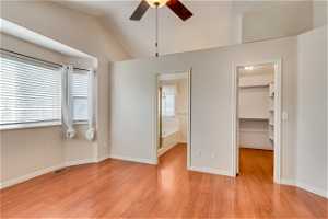 Unfurnished bedroom with ceiling fan, light hardwood / wood-style flooring, ensuite bath, a spacious closet, and vaulted ceiling