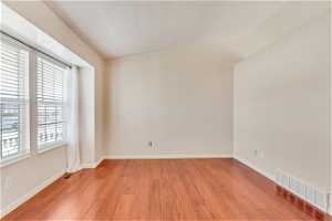 Unfurnished room with a healthy amount of sunlight, vaulted ceiling, and light hardwood / wood-style floors