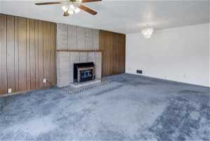 Unfurnished living room featuring dark carpet, ceiling fan with notable chandelier, and a fireplace